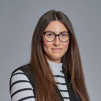 Donna con occhiali e maglia a righe su sfondo grigio.