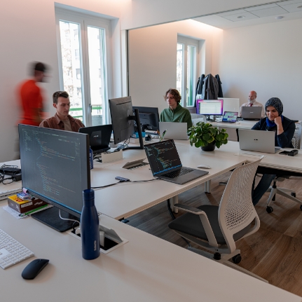 Ufficio moderno con persone al lavoro, computer e piante su scrivania.