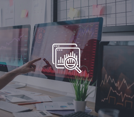 Analisi dei Dati Finanziari su Schermi Persona che indica un grafico finanziario su un monitor in un ufficio con documenti ed elementi decorativi sulla scrivania.